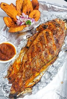 an image of fish on tin foil with sauces and french fries in the background