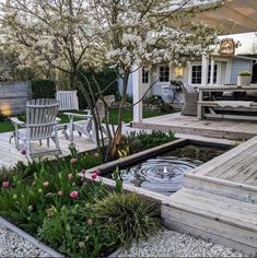 a deck with chairs and water feature in the center, surrounded by plants and flowers