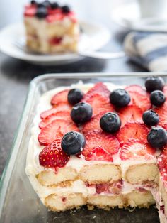 a cake with strawberries and blueberries on top is in a glass pan, ready to be eaten