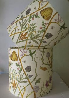 two lampshades with floral designs on them sitting on a white tablecloth covered surface