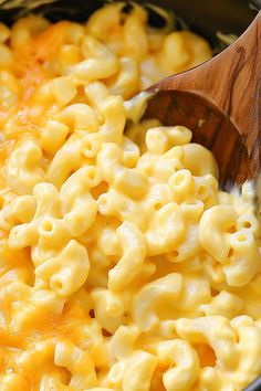 macaroni and cheese is being stirred with a wooden spoon in a crock pot