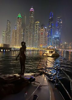 a woman standing on the back of a boat in front of a city at night