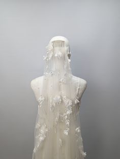 the back of a white wedding dress with flowers on it's neck and veil