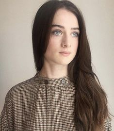 a woman with long hair wearing a brown and black checkered shirt looking at the camera