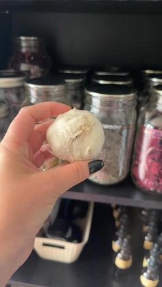 a person holding up a piece of garlic in front of some jars with other spices