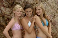 three beautiful young women in bikinis standing next to a rock wall and posing for the camera