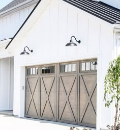 a white house with two garage doors and three lights on each side of the door