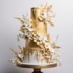 a gold and white wedding cake with flowers on top