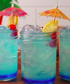 three mason jars filled with blue liquid and lemon wedges next to each other on a table