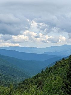 the mountains are covered in green trees and clouds as seen from an overlook point on a cloudy day