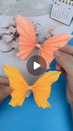 two hands are holding origami butterflies on a table