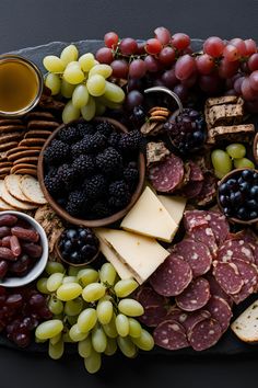 an assortment of cheeses, crackers and grapes on a platter