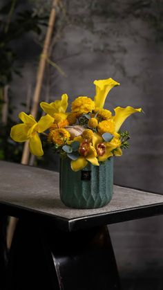 a green vase filled with yellow flowers on top of a table