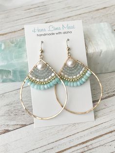 a pair of gold hoop earrings with blue beads and pearls on them sitting on top of a card