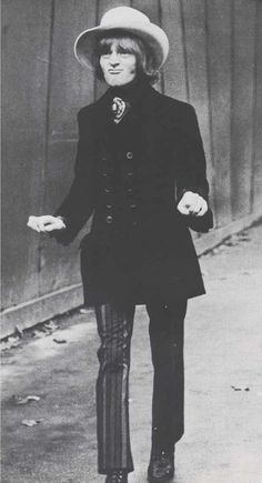 an old black and white photo of a woman in a hat walking down the street