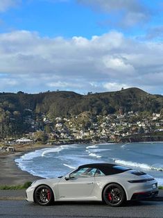 a white sports car parked on the side of a road next to the ocean and houses