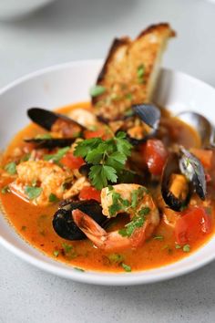 a bowl of seafood soup with bread and garnish on the side, ready to be eaten