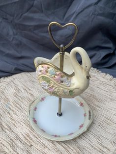 a white swan figurine sitting on top of a saucer with a heart shaped handle