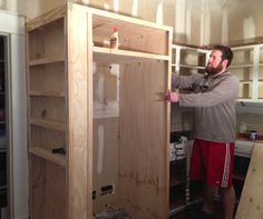 a man standing next to a wooden cabinet in a room with unfinished walls and shelves