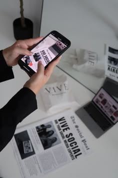 a person holding a cell phone in their hand while sitting at a table with magazines on it