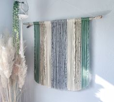 there is a wall hanging made out of strips of yarn and some plants next to it