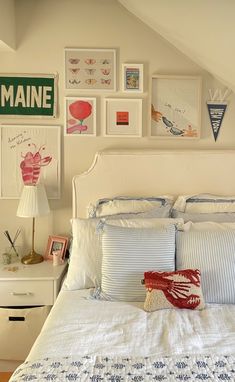 a white bed topped with lots of pillows next to a wall filled with framed pictures