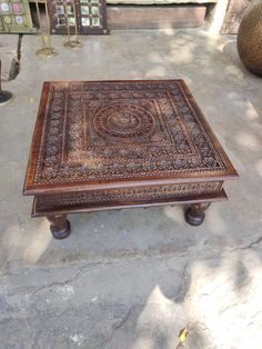 a wooden table with intricate carvings on the top and bottom, sitting in front of other items