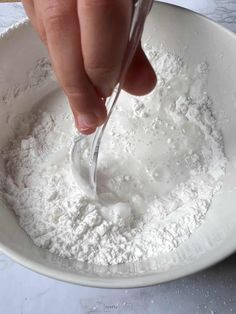 a person spooning flour into a white bowl