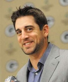 a man in a suit smiles at the camera while wearing a blue and white checkered shirt