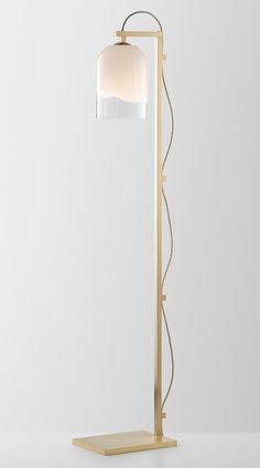 a floor lamp with a white shade on the top and a gold metal base, against a light gray background