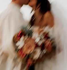 two people kissing each other in front of a white wall with red and orange flowers