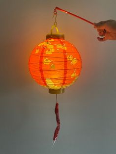 a person holding a string attached to a paper lantern hanging from the ceiling with an orange and yellow design on it