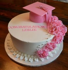 a white cake with pink flowers and a graduation cap on top