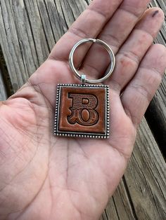 a hand holding a brown leather keychain with the letter g on it