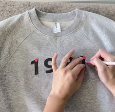 two hands on top of a gray sweatshirt with the number thirteen printed on it and one hand holding a pink crayon pencil