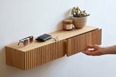 a wooden shelf with sunglasses, cell phone and other items on it next to a potted plant