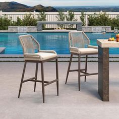 two chairs sitting next to each other near a swimming pool with an outdoor dining table and bar stools