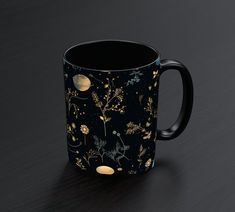 a black coffee mug with gold flowers and planets printed on the inside, sitting on a dark surface