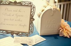 a blue table topped with a white box and flowers next to a sign that reads, please send the bride and groom