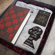 an open box containing two t - shirts, one with a woman's face and the other with red leaves