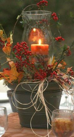 a candle is lit in a vase with flowers and leaves around it, surrounded by orange daisies