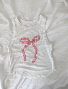 a white tank top with a pink bow on the front and back, sitting on a bed