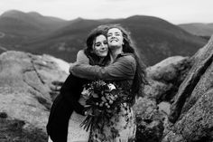 two women hugging each other on top of a mountain