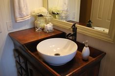 a white bowl sink sitting on top of a wooden counter next to a bathroom mirror