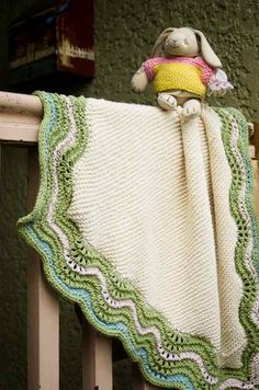 a crocheted blanket with a stuffed animal on it sitting on top of a wooden rail