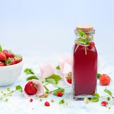 a bottle of strawberry syrup next to a bowl of strawberries on a white surface