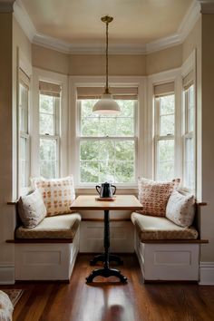 a window seat with pillows on it next to a table