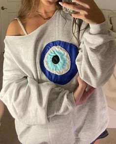 a woman is taking a selfie with her cell phone while wearing an eye sweatshirt