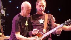 two men standing next to each other holding guitars