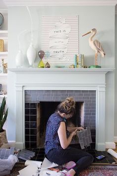 a woman sitting on the floor in front of a fire place holding a tile block